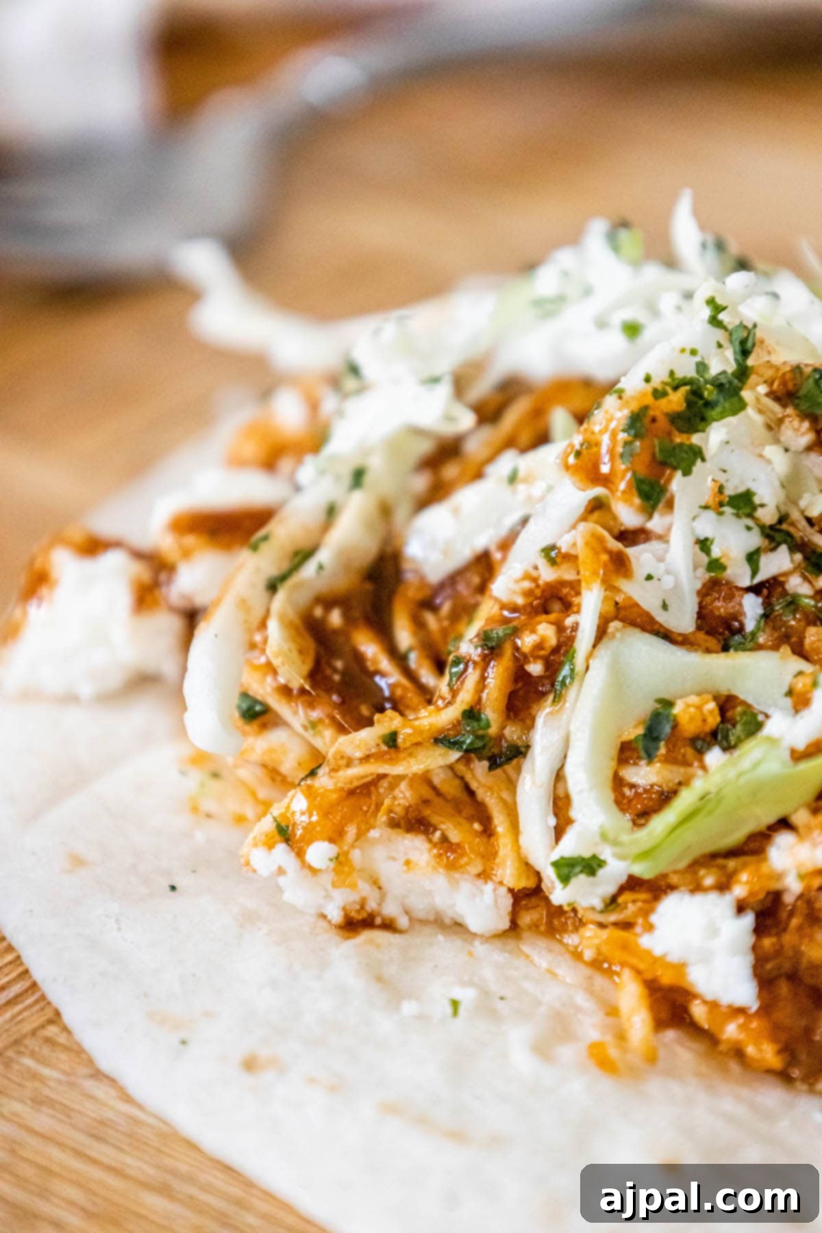 shredded chicken tinga in a tortilla with chopped cilantro, cabbage, and crumbled cotija cheese on top