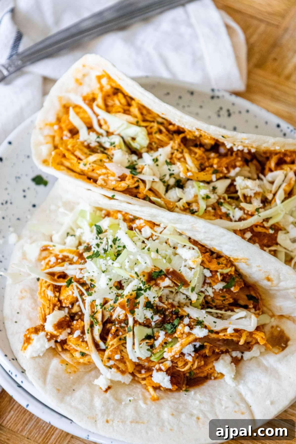 shredded chicken tinga in a tortilla with chopped cilantro, cabbage, and crumbled cotija cheese on top