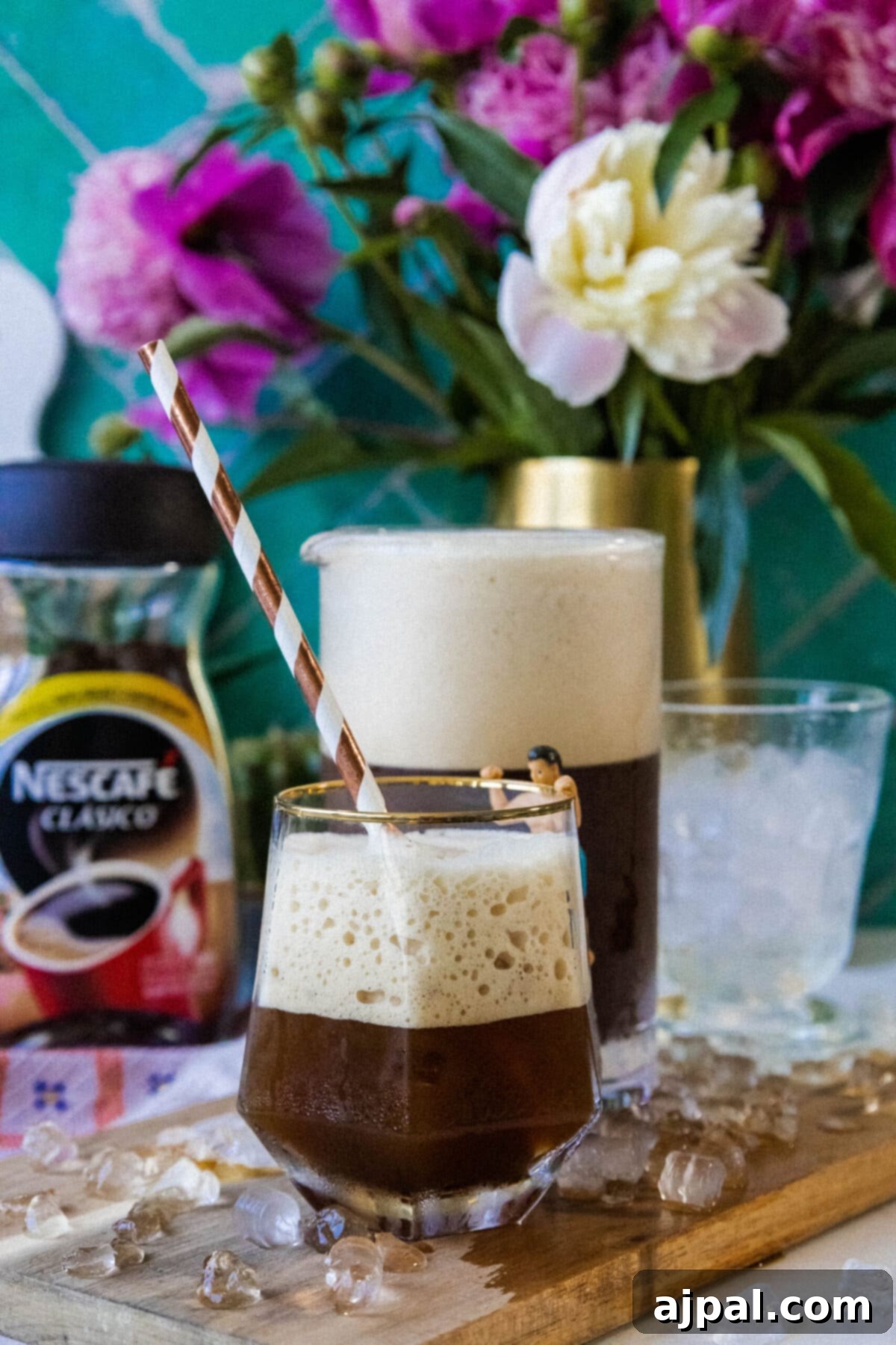 Whipped Greek frappé coffee in a glass with ice and foam and a paper straw on a table