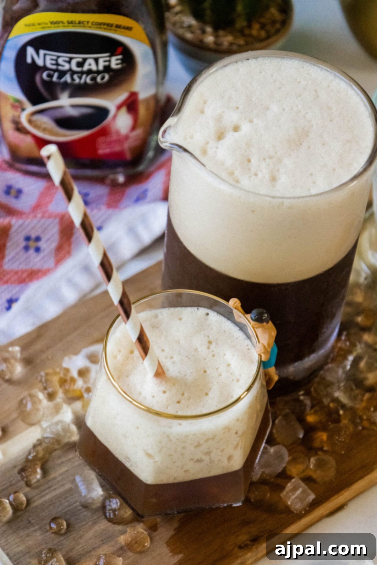Whipped Greek frappé coffee in a glass with ice and foam and a paper straw on a table