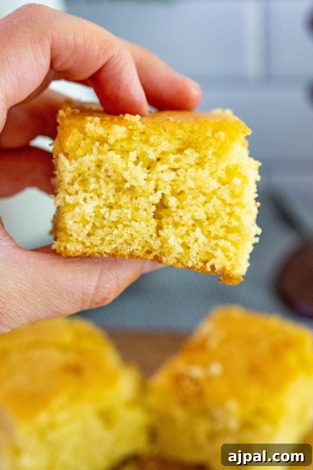 A person proudly holds up a perfect slice of honey butter cornbread, showcasing its moist interior and golden crust.
