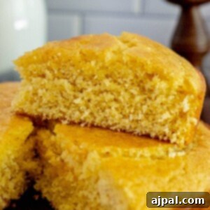 A wedge of honey butter cornbread sliced and placed on top of the loaf of cornbread on a table