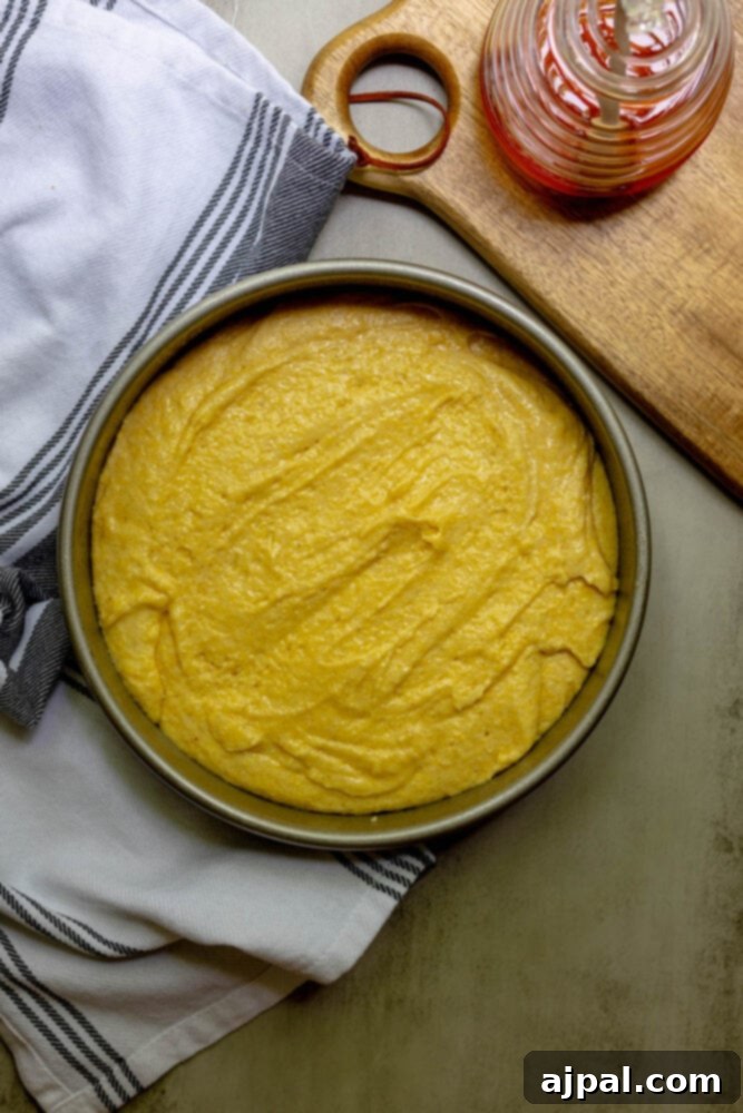 A smooth, golden cornbread batter is carefully poured into a greased baking pan, ready for the oven.