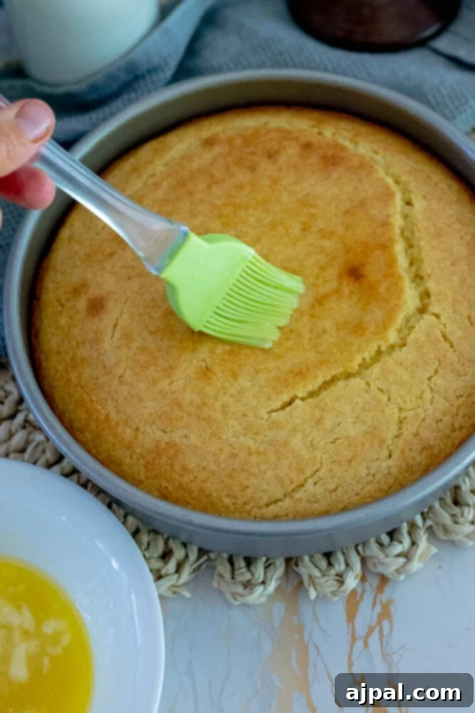 Freshly baked cornbread, golden and warm in its pan, is generously brushed with a shimmering honey butter mixture, creating an enticing glaze.
