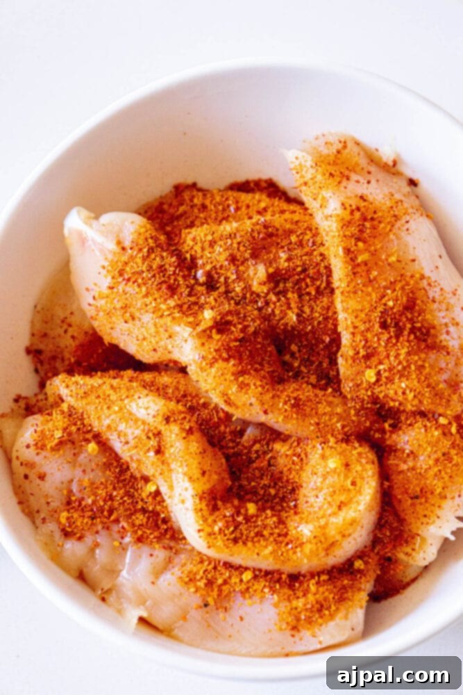 Raw chicken tenders in a bowl with Ajika seasoning, illustrating the initial step of the marination process.