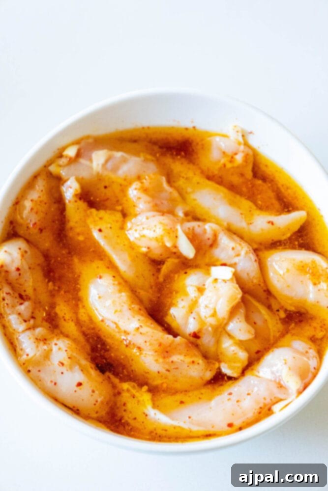 Raw chicken tenders thoroughly coated in Ajika seasoning and olive oil, ready for marination.