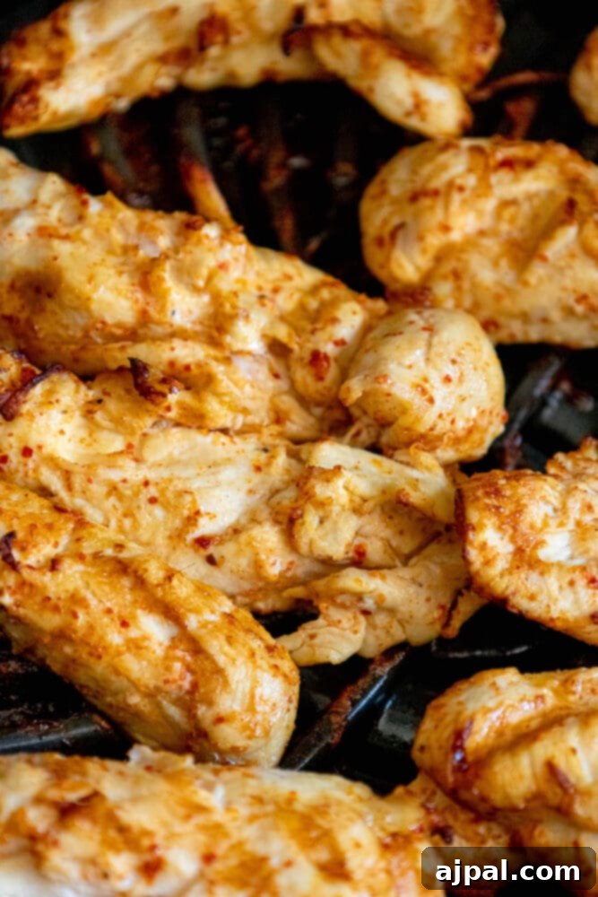 Chicken tenders cooking on a hot grill, sizzling as the Ajika seasoning caramelizes.