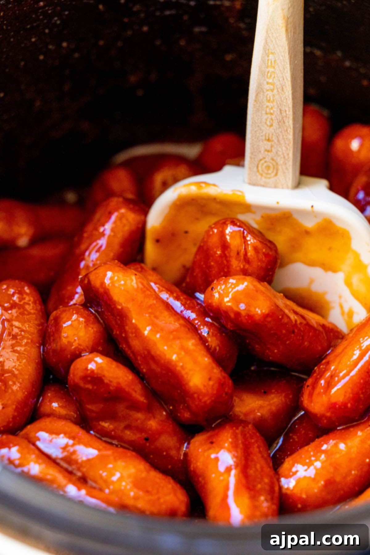 little smokies in bbq sauce in a crock pot with a spatula in the middle