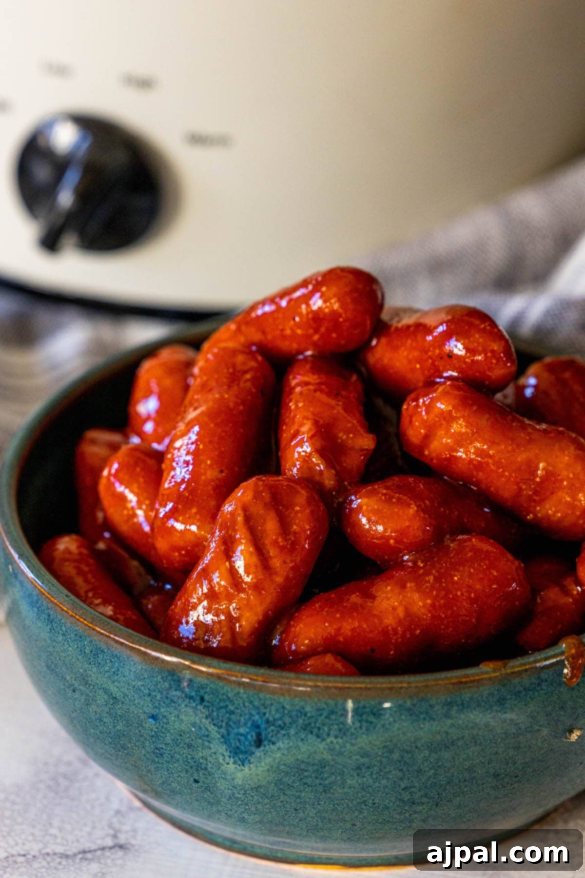 little smokies in bbq sauce in a blue bowl in front of a crock pot on a table