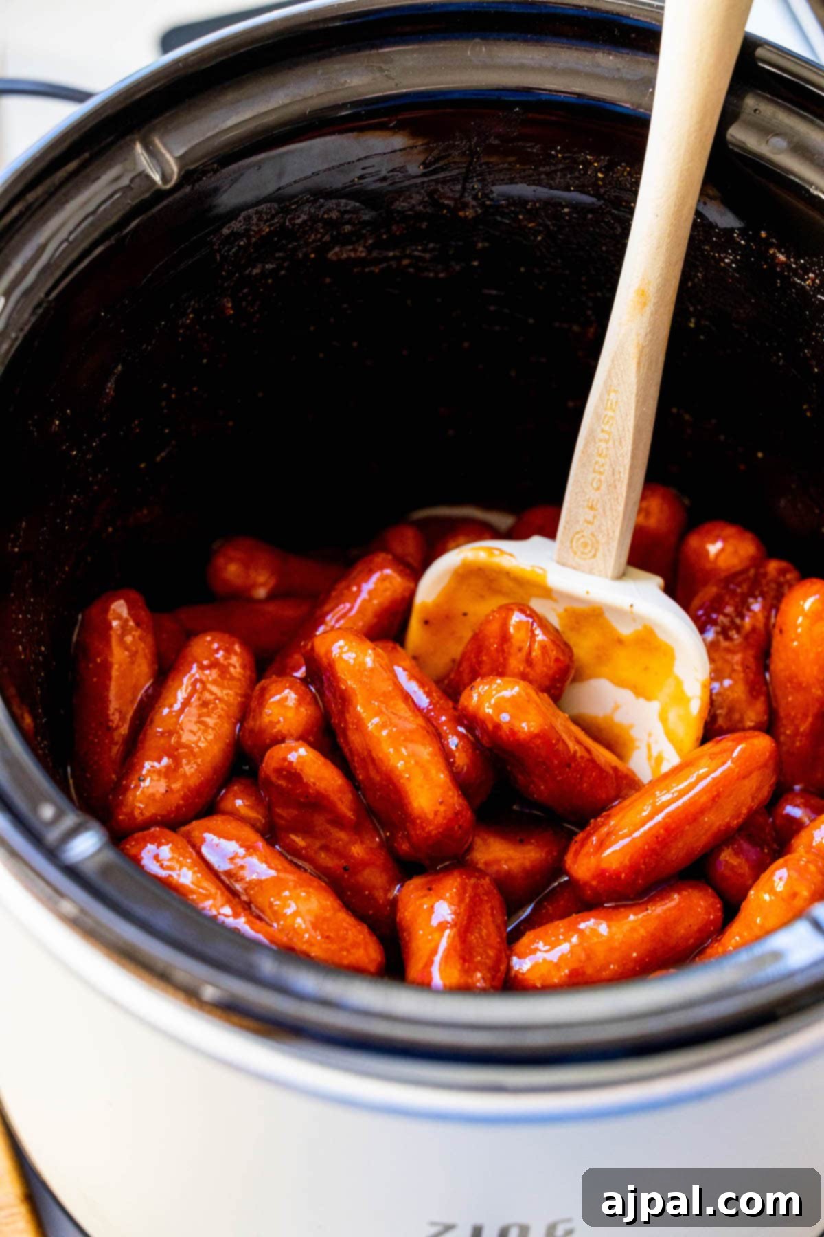 little smokies in bbq sauce in a crock pot with a spatula in the middle