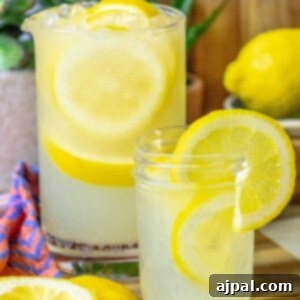 A vibrant glass jar filled with the best homemade lemonade, adorned with a fresh lemon slice and pebble ice, ready for a refreshing sip.