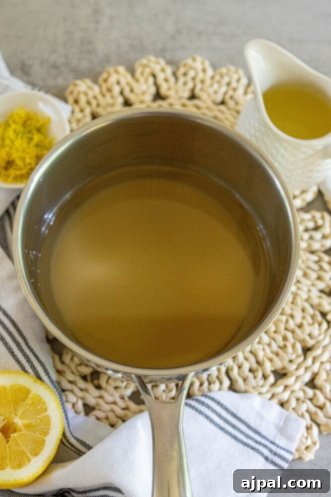 A saucepan on a stovetop, containing a simmering simple syrup, showing the preparation step for making homemade lemonade.