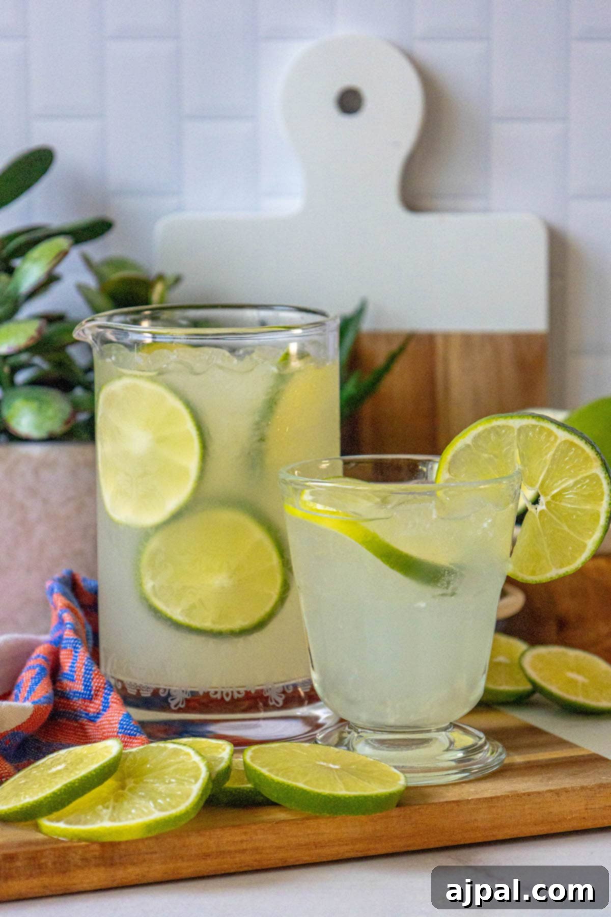 A pitcher of homemade limeade garnished with lime slices, served on a rustic cutting board.