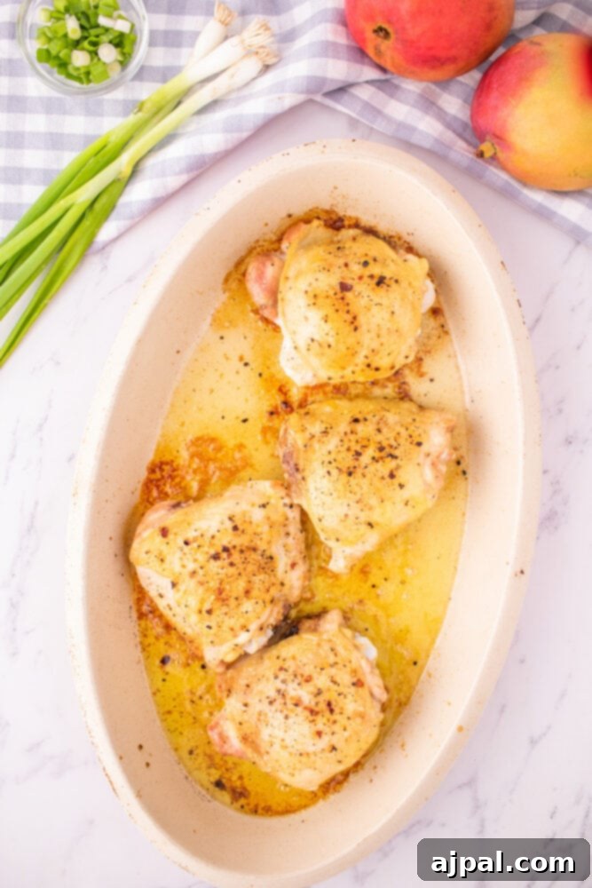 Golden-brown baked chicken thighs, fresh out of the oven, are arranged in a baking dish, showcasing their crispy skin and readiness for the mango chutney.