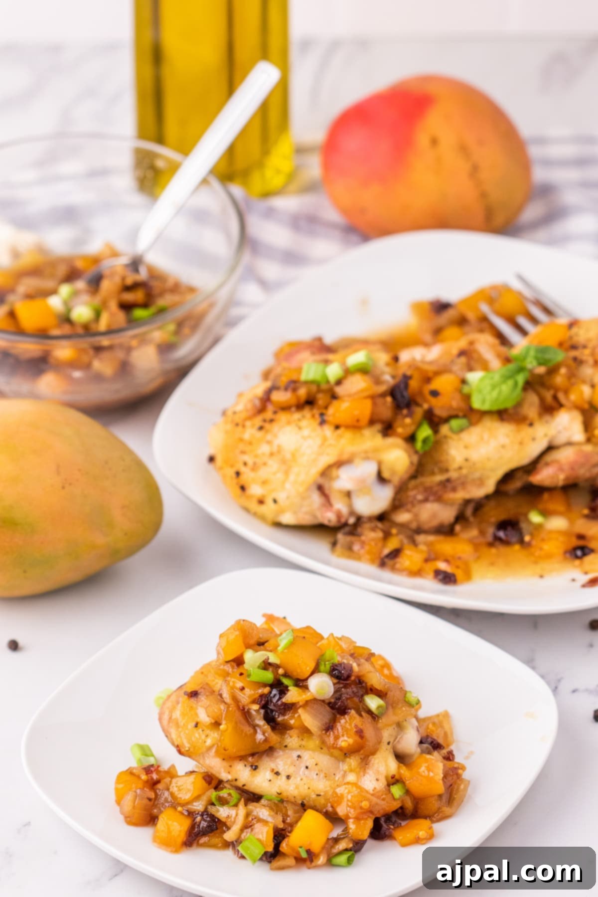 Two white plates, each presenting a perfectly baked chicken thigh generously coated in vibrant mango chutney and garnished with fresh green onions, ready for a delightful meal.