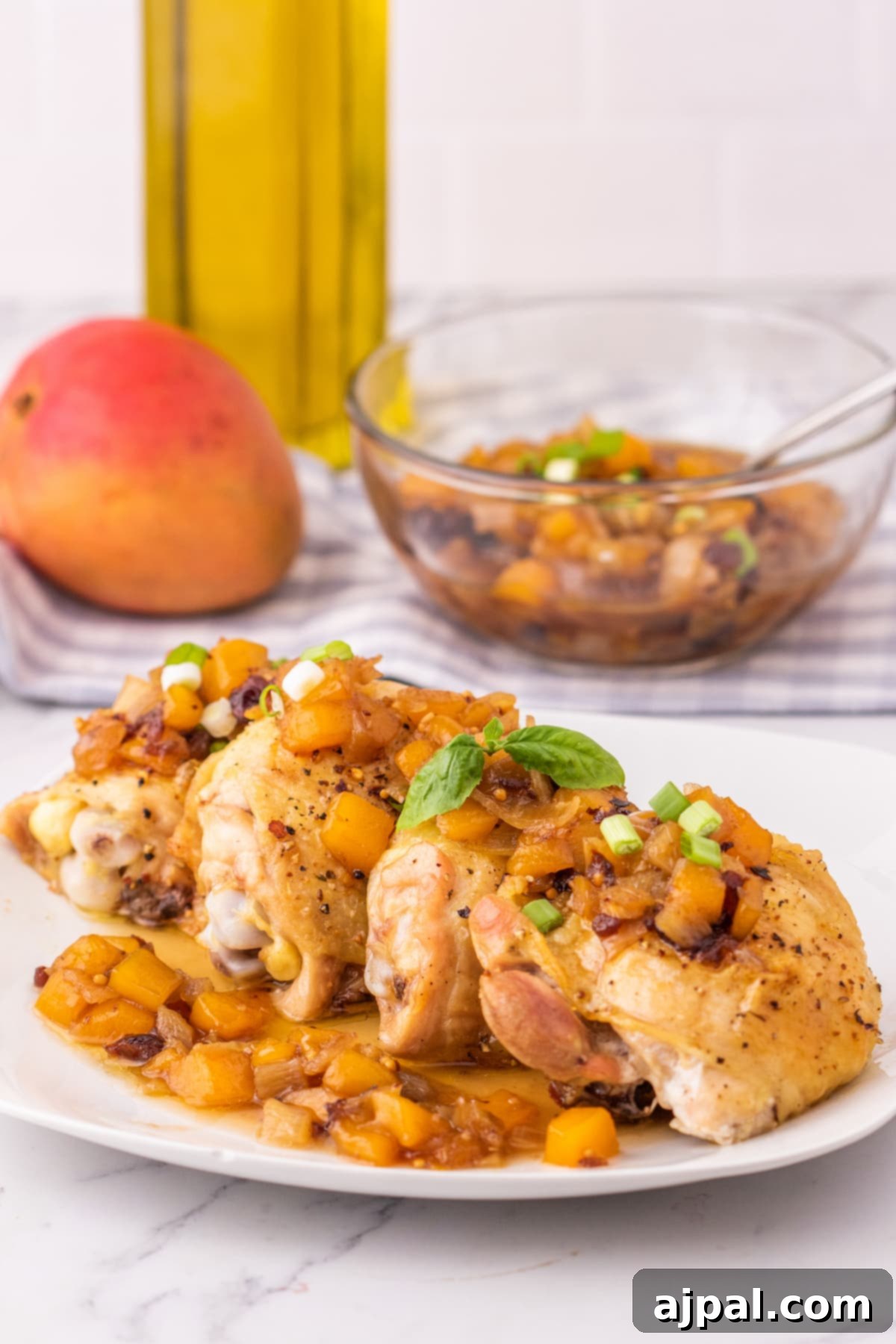 Close-up of baked chicken thigh on a white plate, generously covered in mango chutney and garnished with sliced green onions, ready to be served.