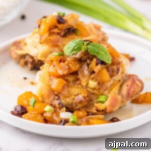 Baked chicken thigh on a white plate covered in mango chutney and sliced green onions