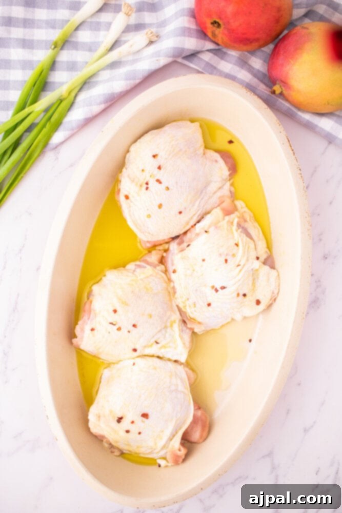 Several raw chicken thighs, glistening with olive oil and seasonings, are shown in a baking dish, prepared for roasting.