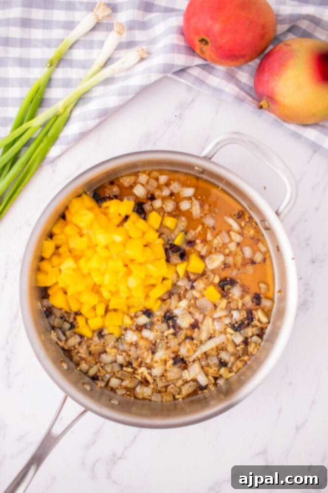 Freshly diced mangoes, aromatic spices, and other chutney ingredients are simmering gently in a pan, beginning to meld into a rich sauce.