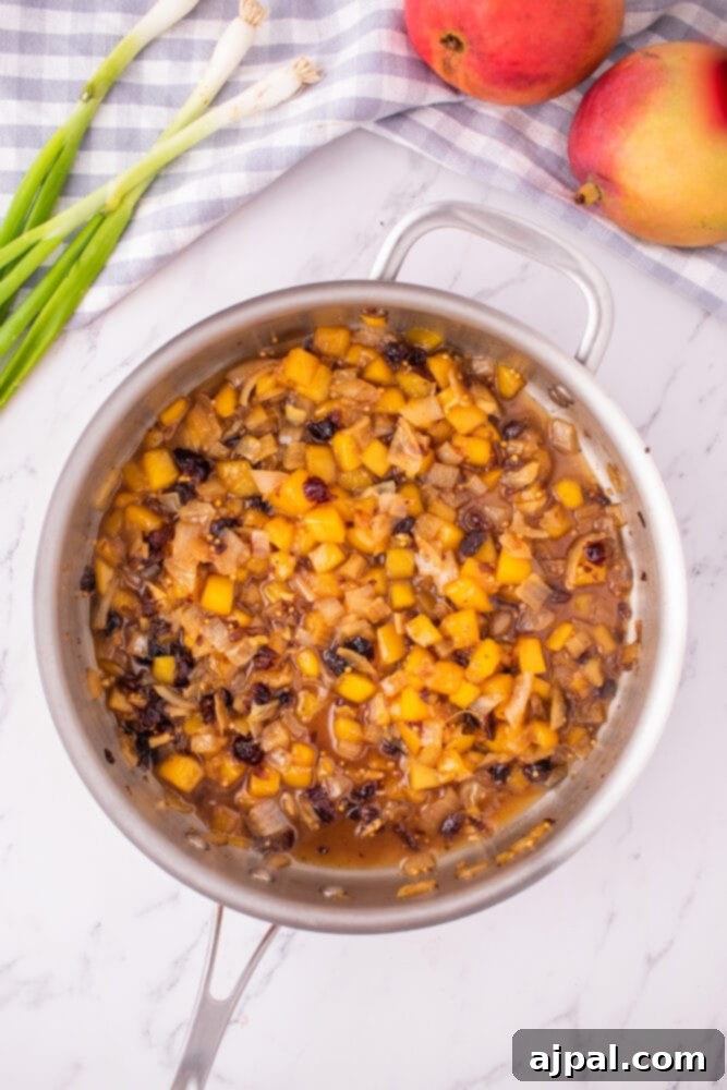 The mango chutney, now thicker and more fragrant, continues to simmer slowly in the pan, allowing its complex flavors to fully develop and deepen.