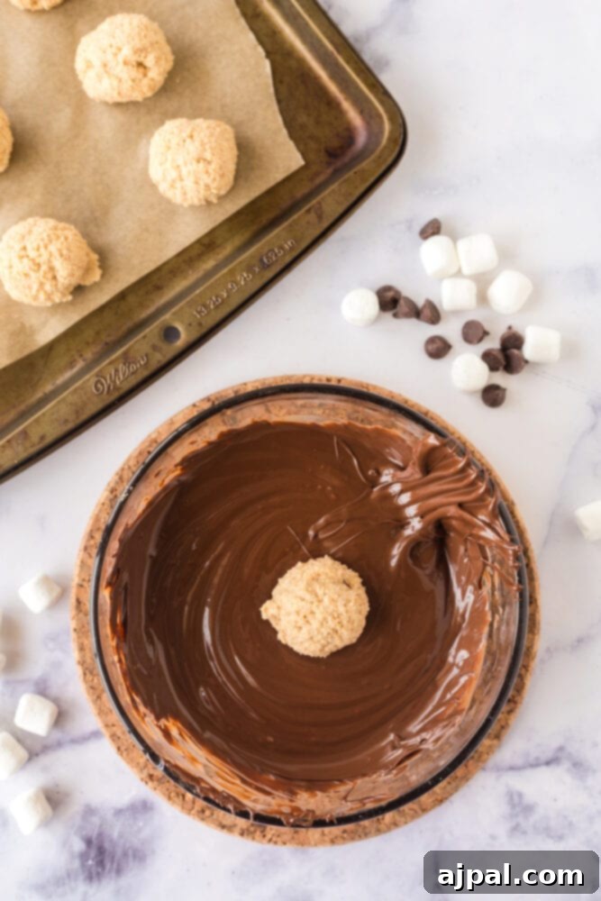 A marshmallow fluff truffle immersed in a bowl of glistening melted chocolate, ready for coating.