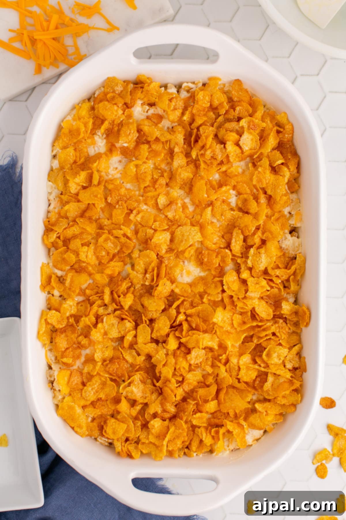 An unbaked funeral potato casserole in a dish, topped with a layer of buttered cornflakes, ready for the oven.