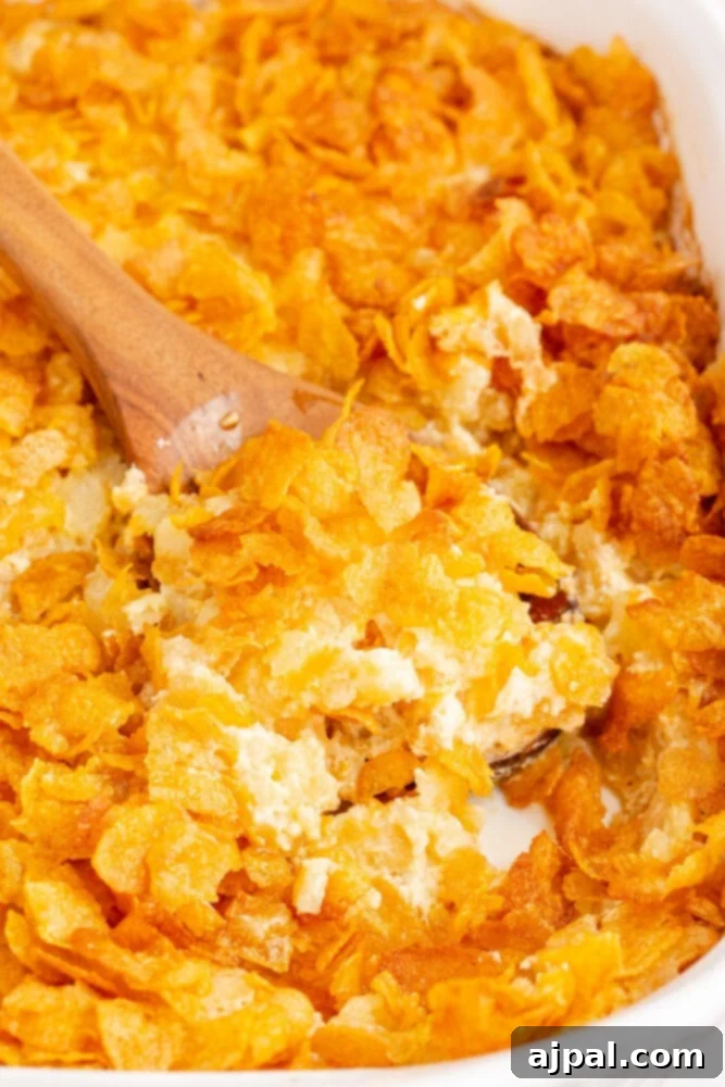 A crunchy funeral potato casserole dish with a wooden spoon in it, showcasing the golden-brown topping and creamy interior.