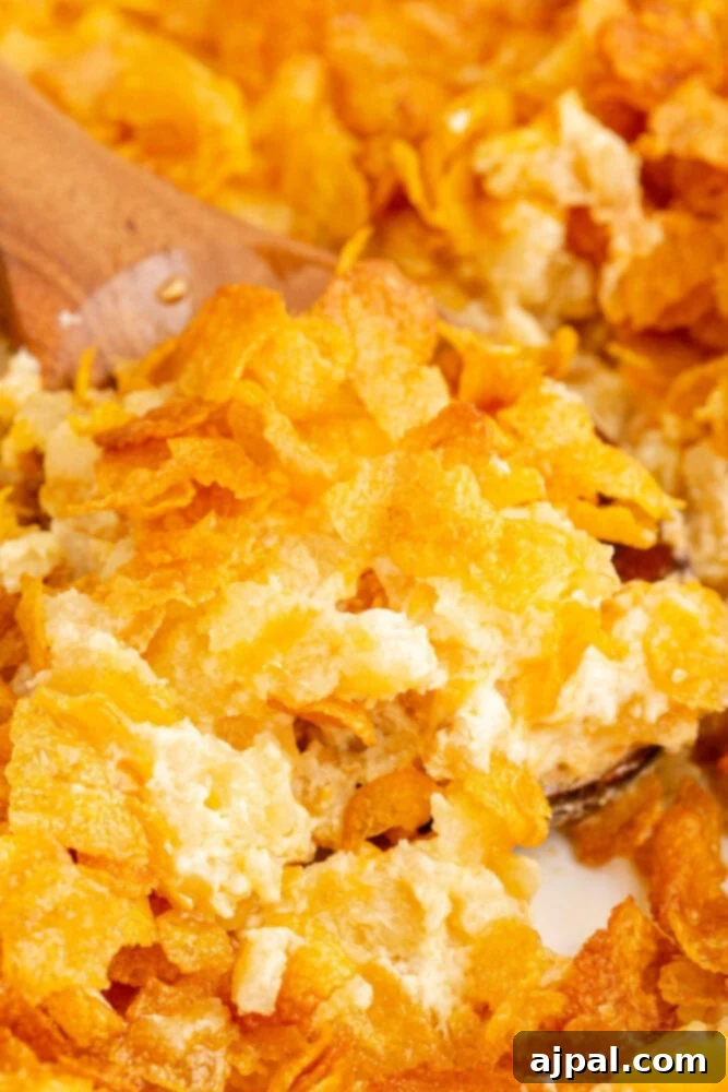 A wooden spoon scooping a generous portion of cheesy hashbrown casserole from a white dish, showing its creamy texture.