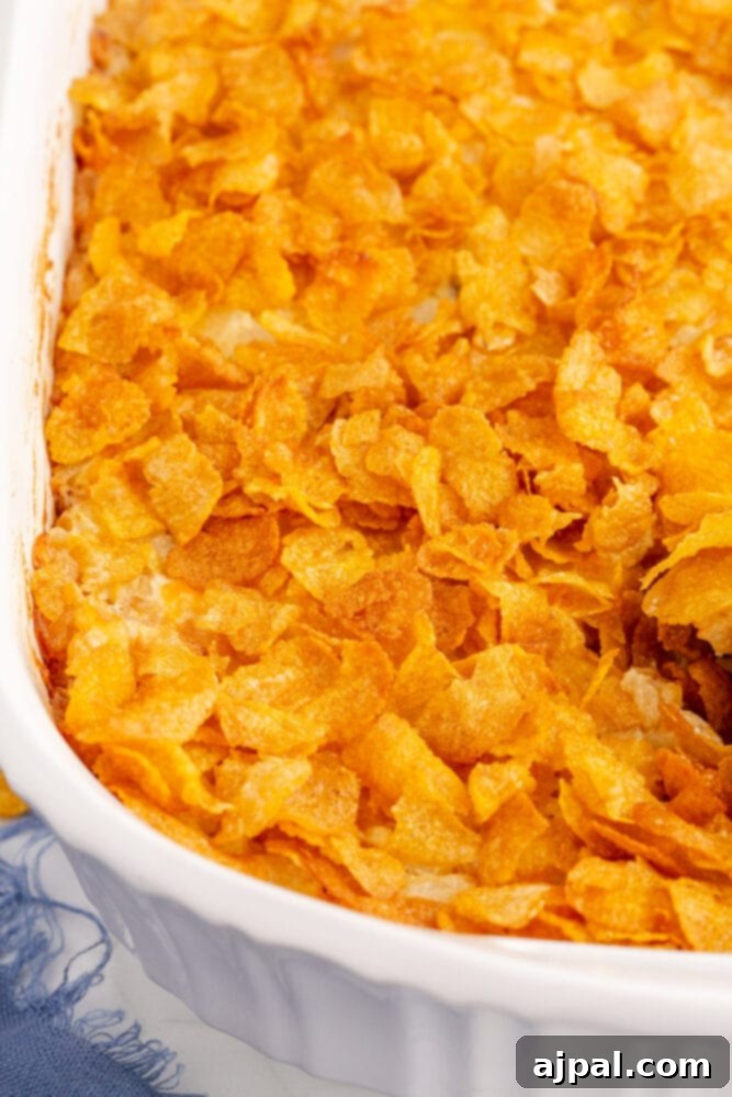 A cheesy hashbrown casserole freshly baked in a rectangular white casserole dish, with a golden-brown cornflake topping.