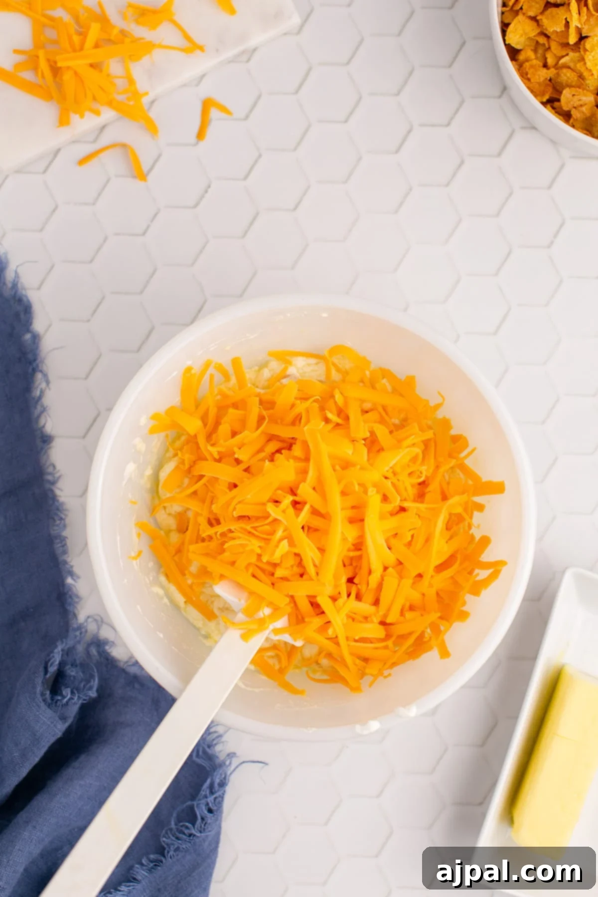 Shredded cheddar cheese being added to the creamy soup and butter mixture in a bowl, before being fully combined.
