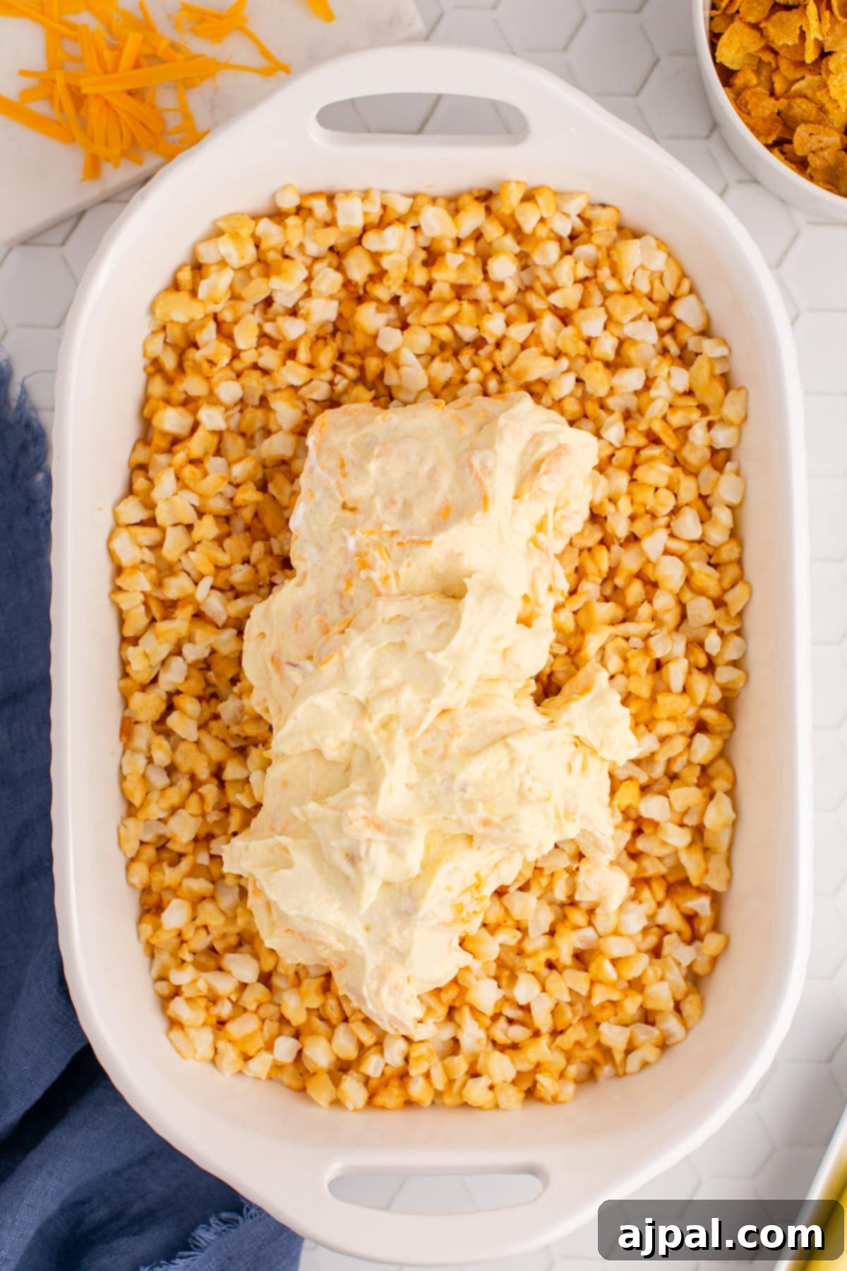 The unbaked hashbrown casserole in a baking dish, with the creamy cheese and soup mixture spread evenly over the potatoes.
