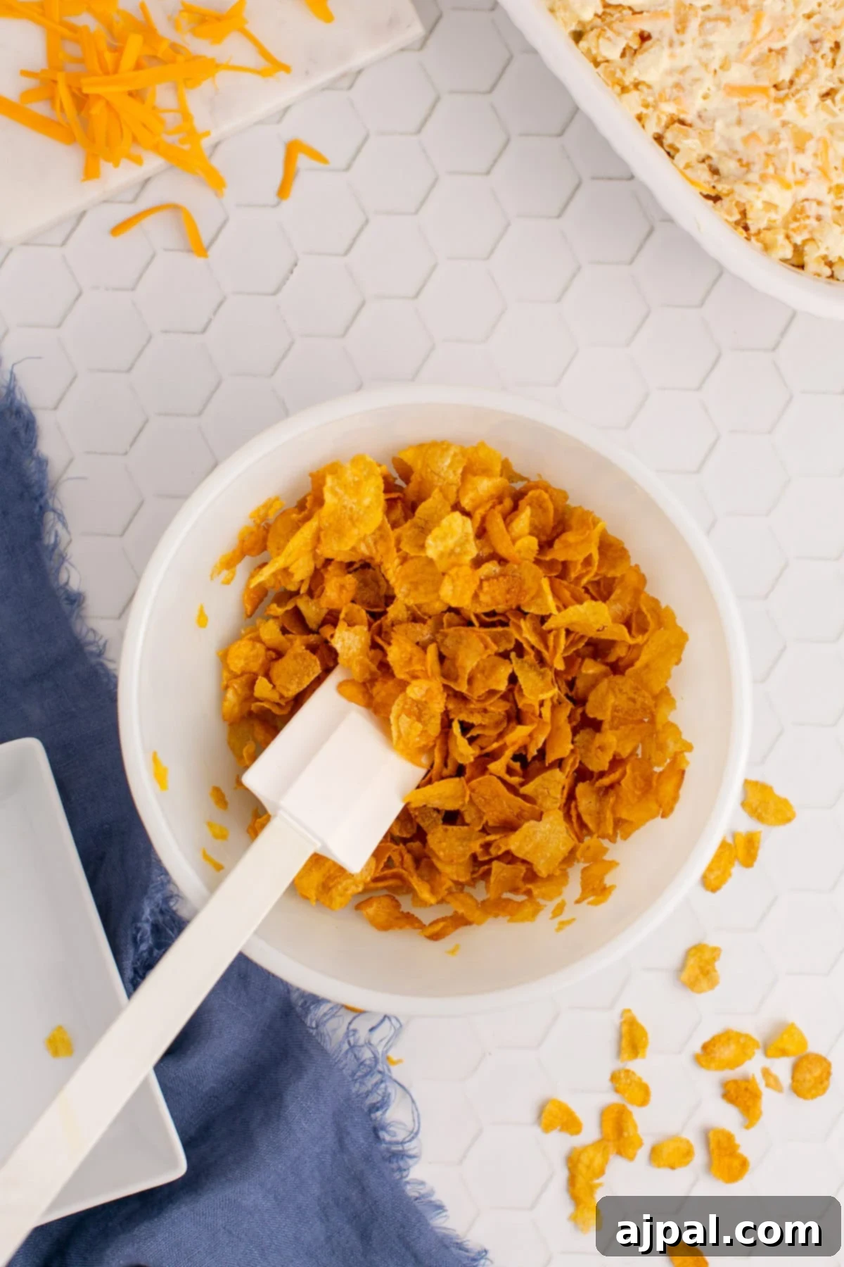 A fork crushing cornflakes in a small bowl, preparing them for the crispy topping of the casserole.