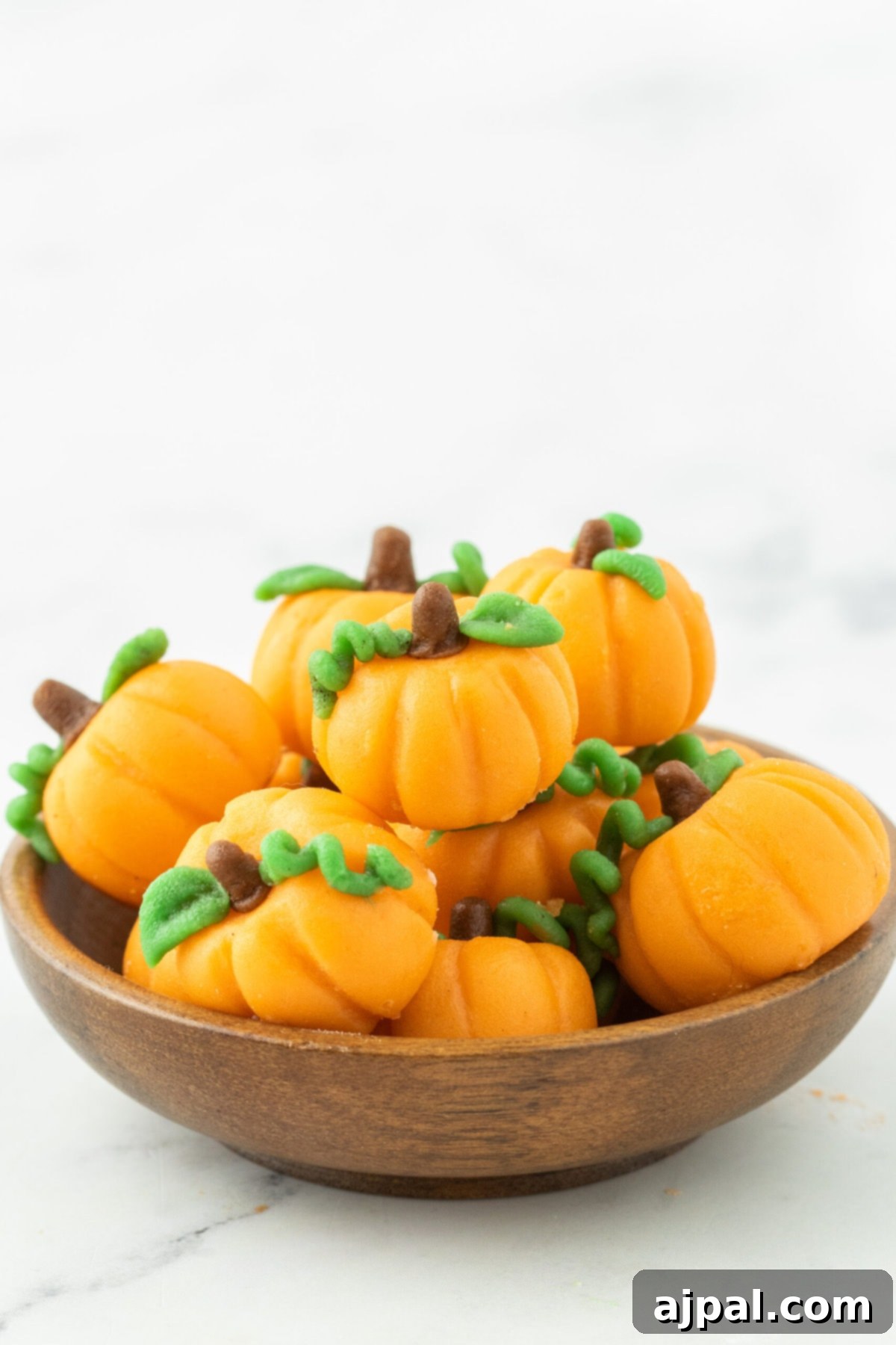 marzipan pumpkin with stem and leaf stacked in a bowl