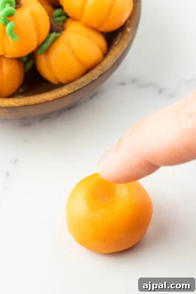 a finger making a small indent on top of a ball or orange marzipan