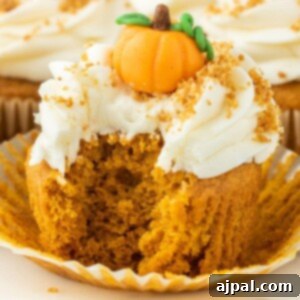 pumpkin cupcake iced with cream cheese frosting and a marzipan pumpkin candy on top