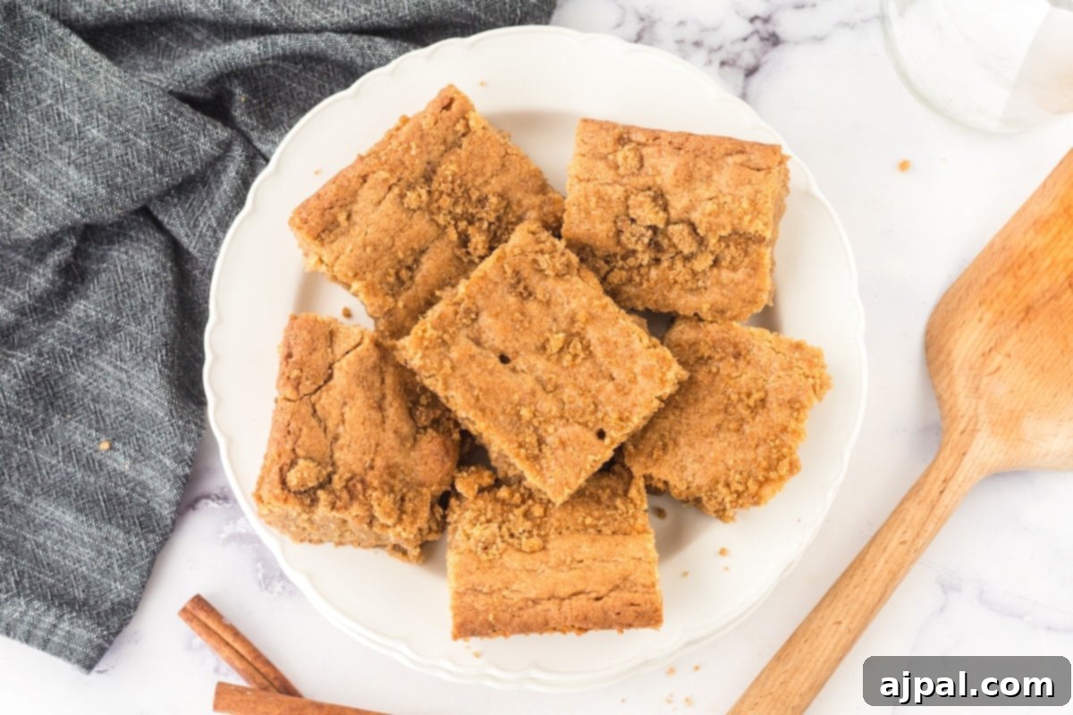A plate featuring a stack of chewy Snickerdoodle Blondies, garnished with a sprinkle of cinnamon, next to a wooden spoon.