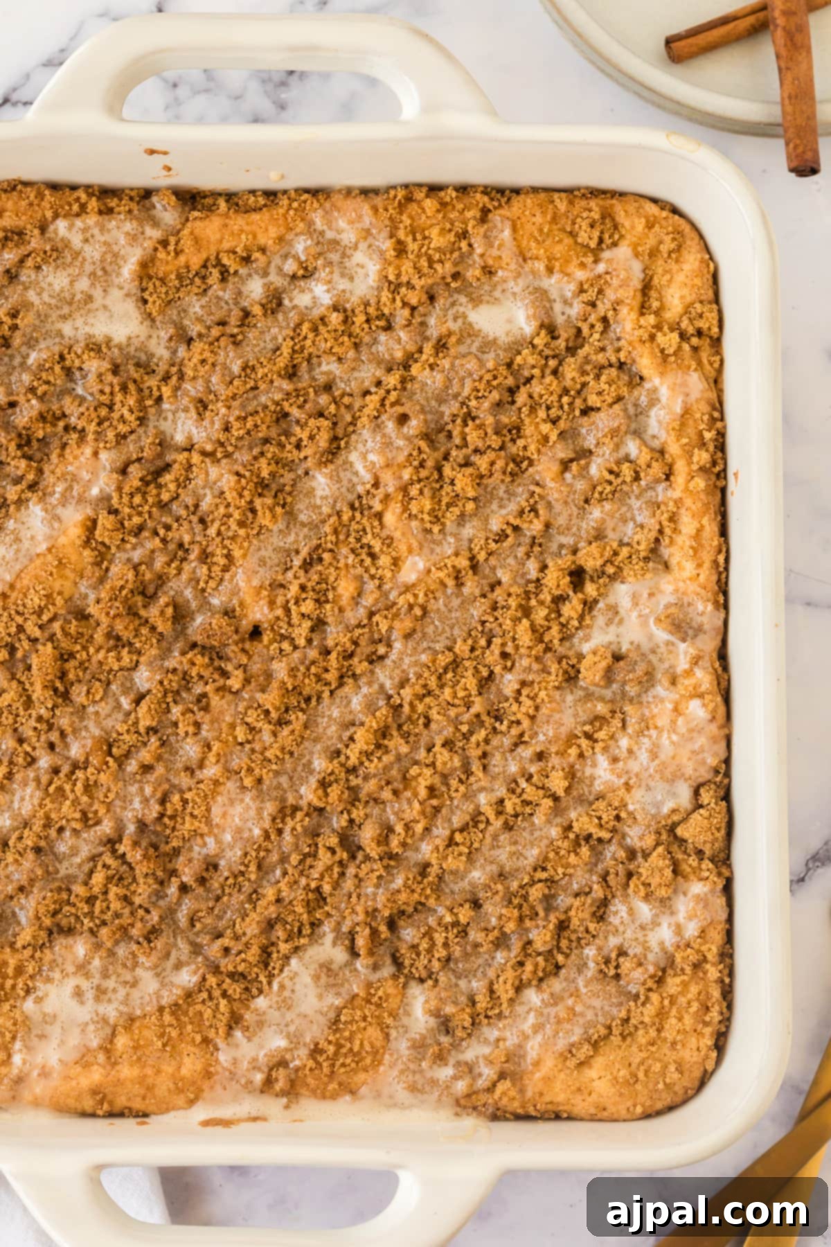 Snickerdoodle Streusel Cake 10 A slice of Snickerdoodle Crumb Cake, still warm and inviting in its dish, adorned with cinnamon sticks, ready to be enjoyed.