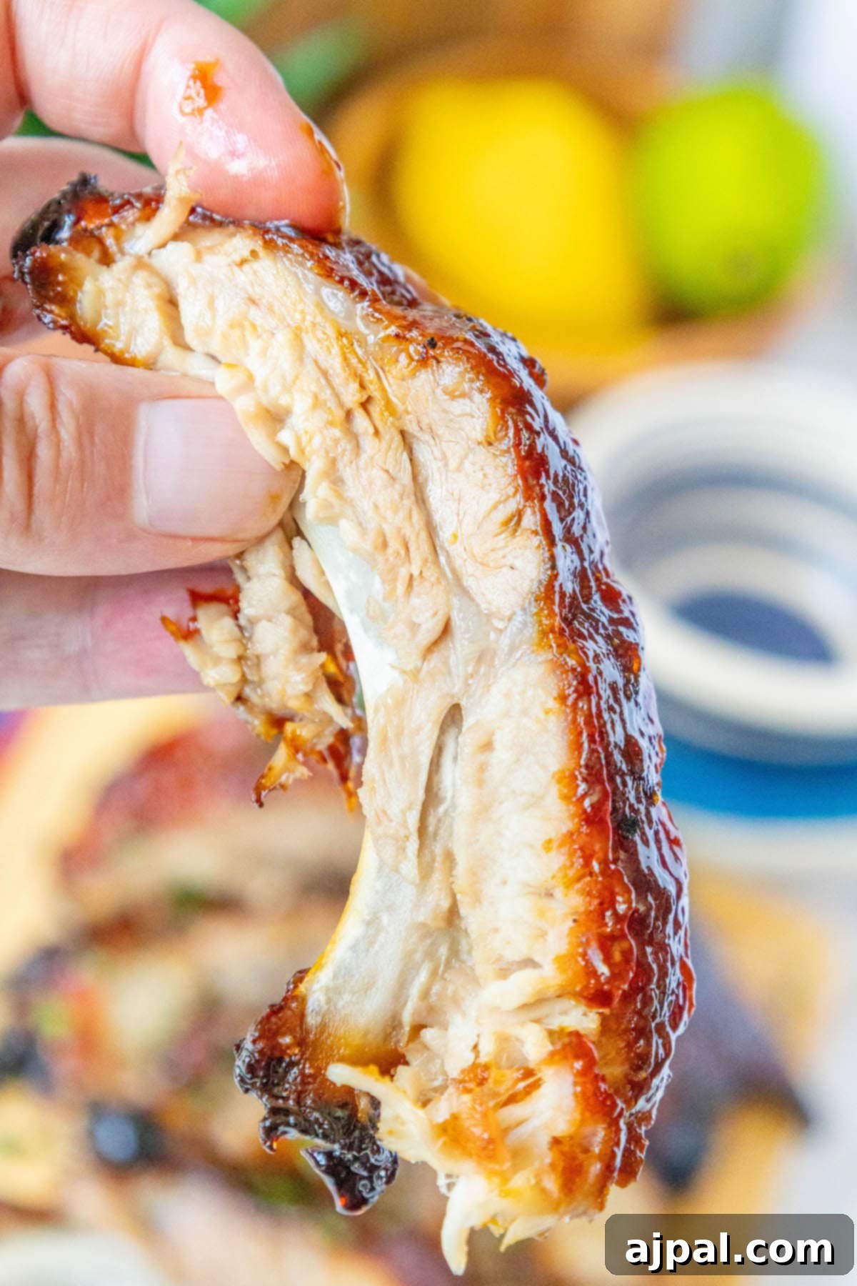 Sweet & Sticky Asian Baked Ribs 2 A hand holding a perfectly baked rib coated in a glossy, sticky Asian glaze, highlighting its tender, melt-in-your-mouth texture, ready to be enjoyed.