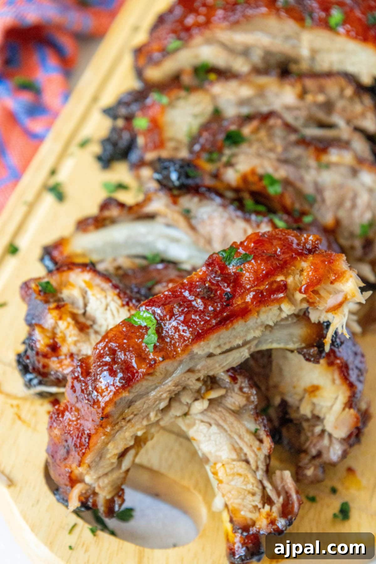 Sweet & Sticky Asian Baked Ribs 3 Baked ribs neatly cut apart and arranged on a rustic wooden plate, glistening with a rich, sticky Asian glaze, highlighting their tender appeal.