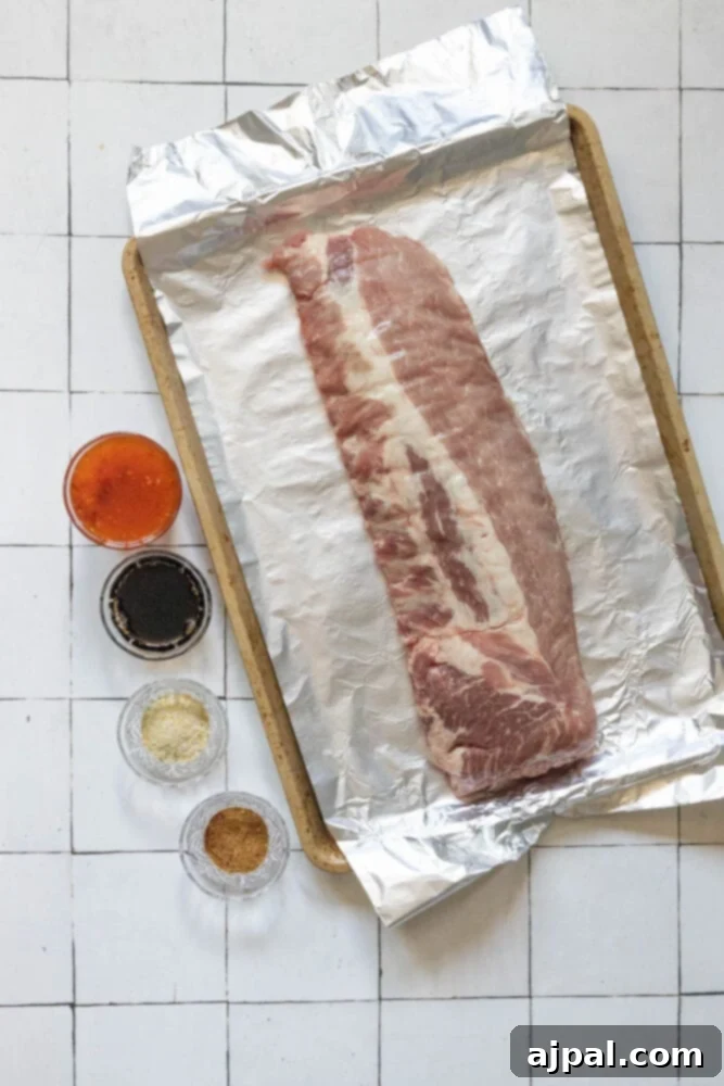 Sweet & Sticky Asian Baked Ribs 4 Rack of ribs on a baking sheet with foil, surrounded by bowls of Asian sauces, fresh herbs, and spices, ready for marinade preparation.
