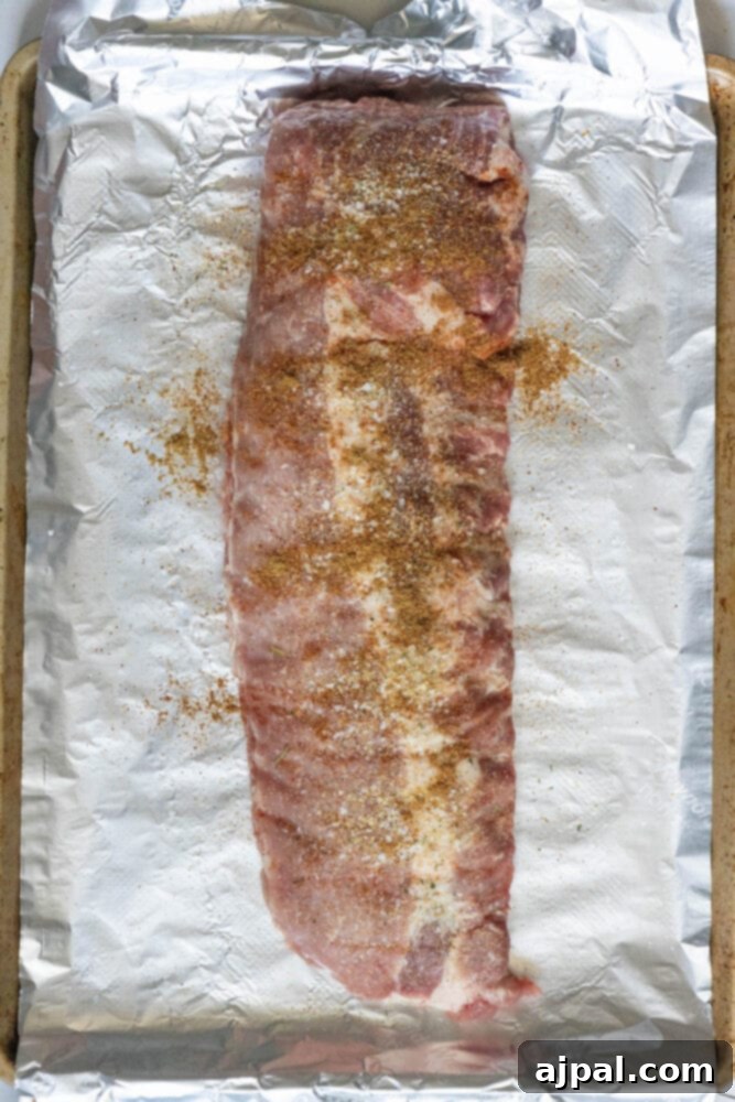 Sweet & Sticky Asian Baked Ribs 5 Seasoned rack of ribs resting on a foil-lined baking sheet, prepared for slow baking in the oven.