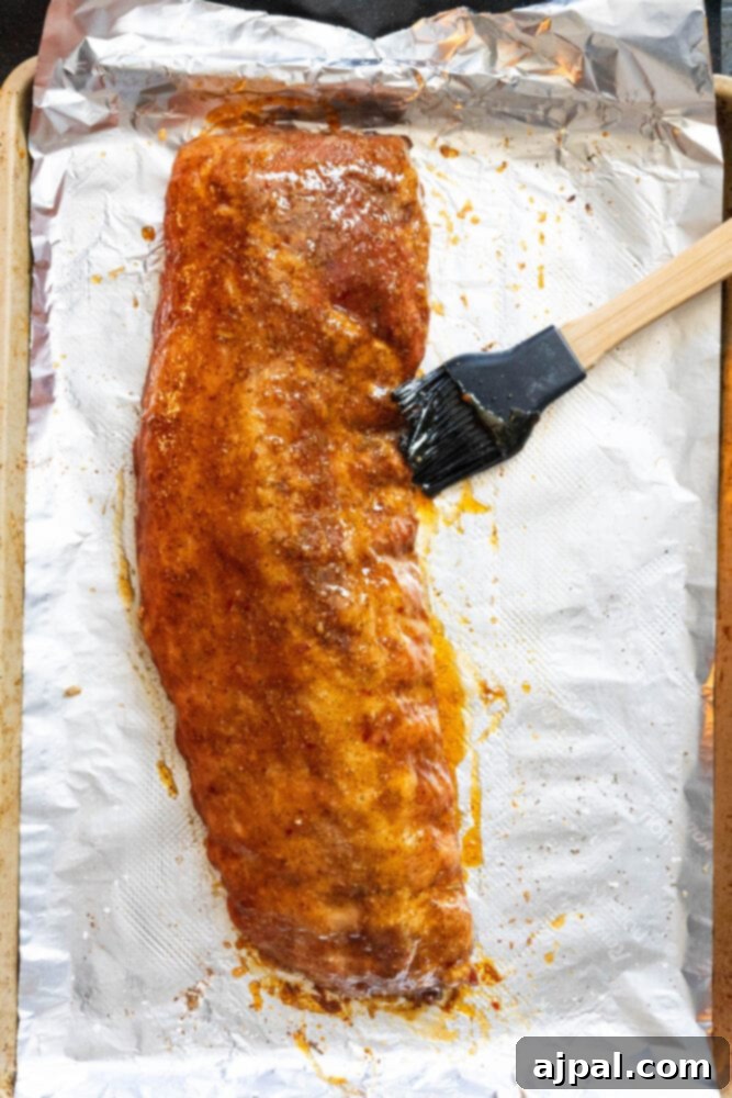 Sweet & Sticky Asian Baked Ribs 6 A cooking brush applying a generous layer of sticky Asian marinade over a rack of ribs, ensuring even coating and maximum flavor.