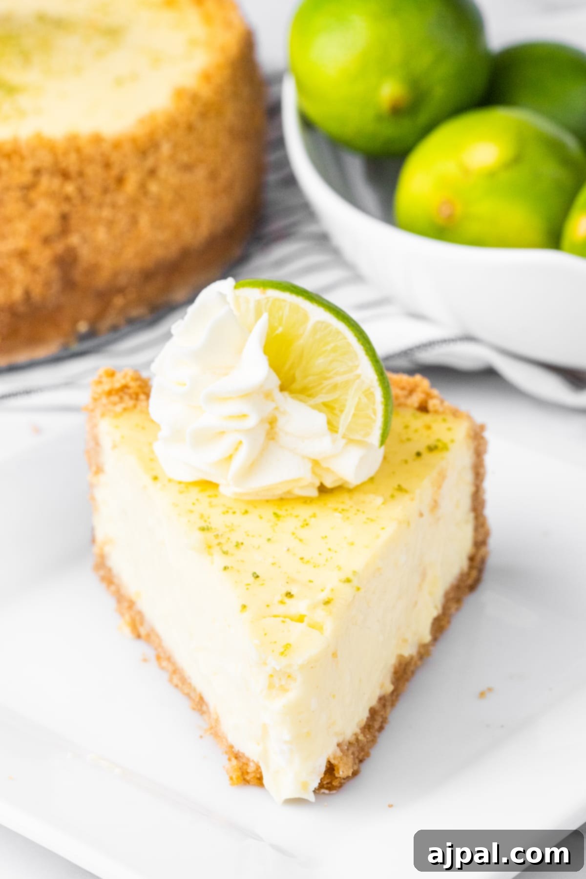 a slice of key lime cheesecake on a plate with a dollop of whipped cream and lime slices on top