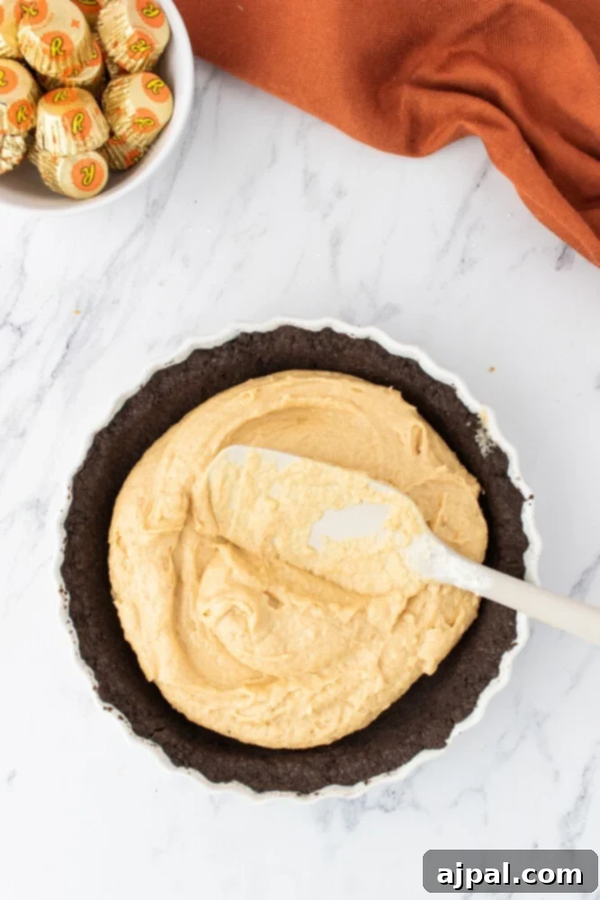 The smooth, creamy peanut butter filling being carefully spread over the baked chocolate pie crust in a pie dish.