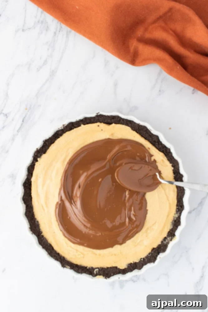 Smooth melted milk chocolate being spread meticulously over the creamy peanut butter filling in a pie dish.