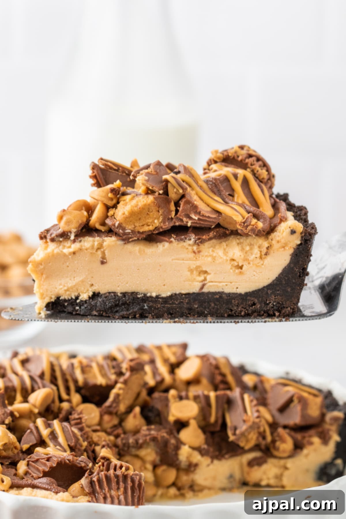 A beautiful slice of peanut butter-filled chocolate crusted pie, topped with mini Reese's cups, being carefully lifted from the whole pie, showing its delicious layers.