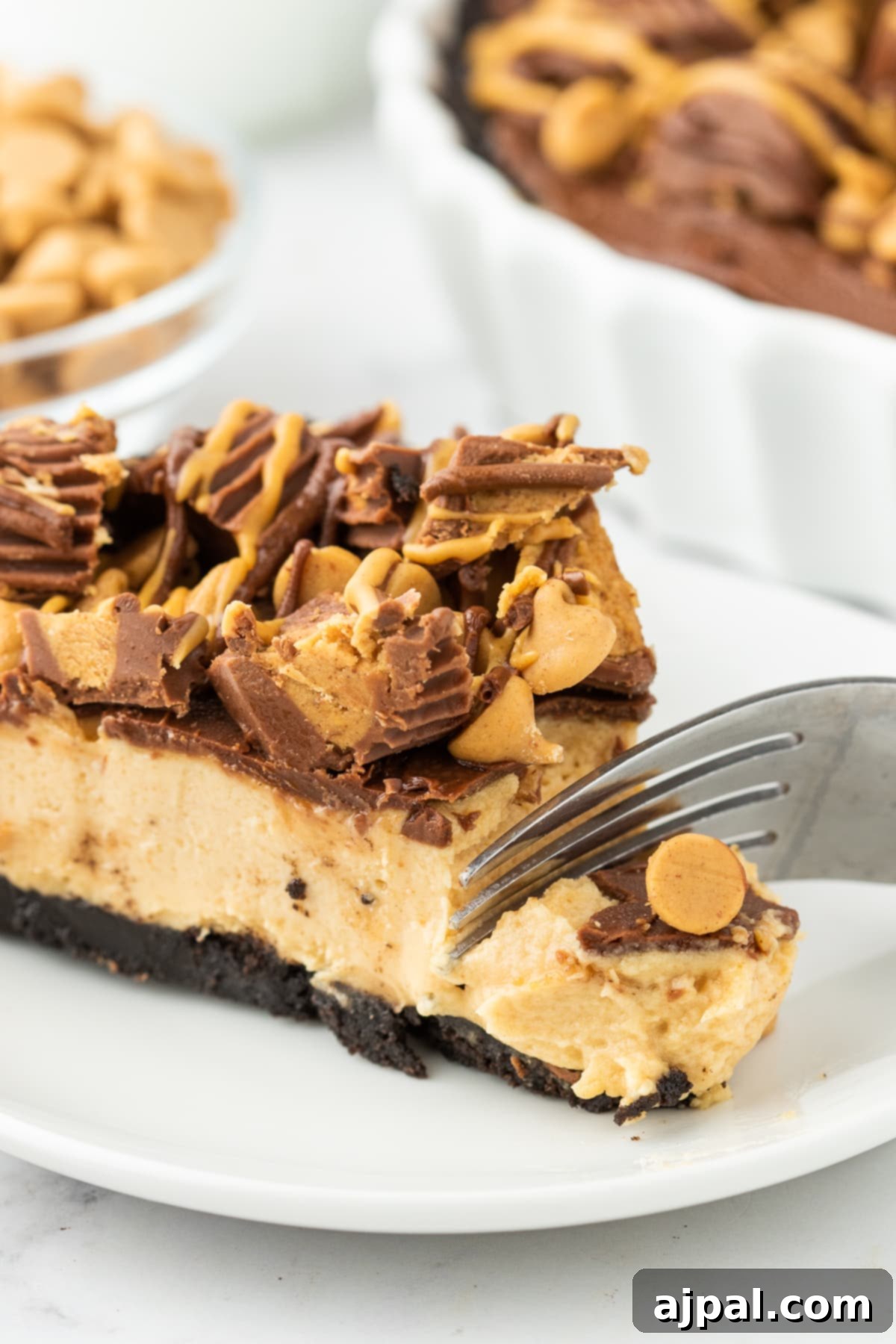 A fork sinking into a slice of Reese's Peanut Butter Pie, showcasing the smooth filling and rich chocolate crust, adorned with peanut butter cups.