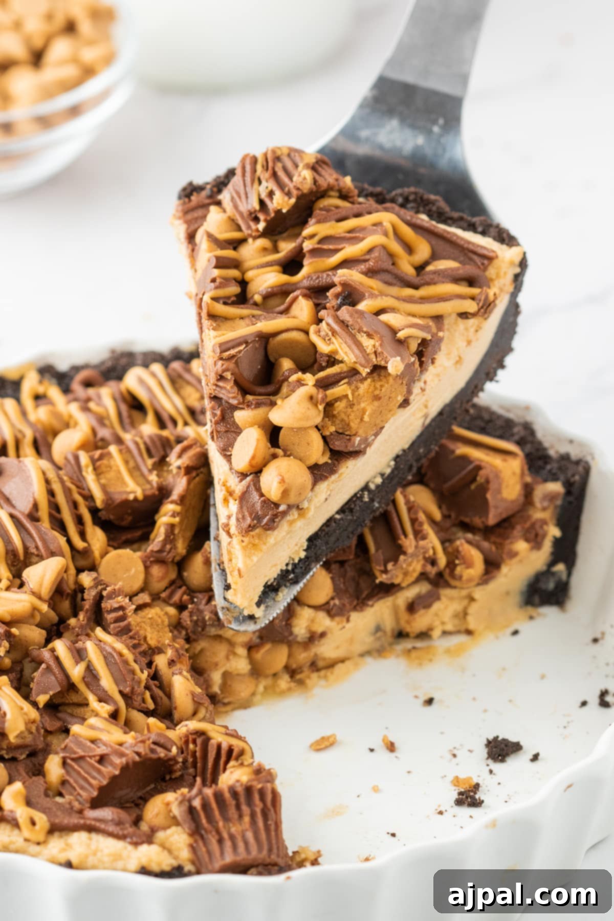 A slice of Reese's Peanut Butter Pie being carefully removed from the whole pie, revealing its layered perfection of crust, filling, and toppings.
