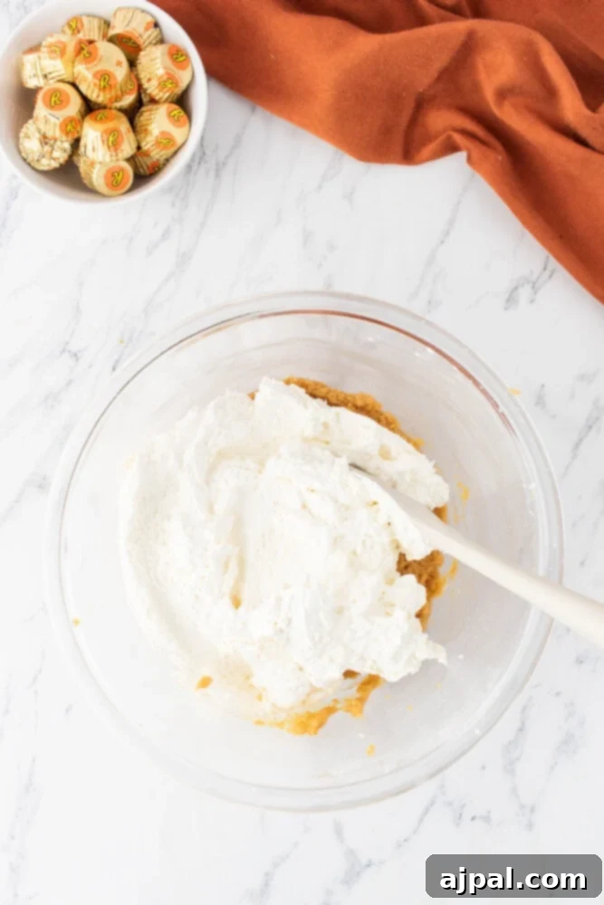 Peanut butter and cream cheese being vigorously mixed together in a bowl with an electric hand mixer, creating a smooth blend.