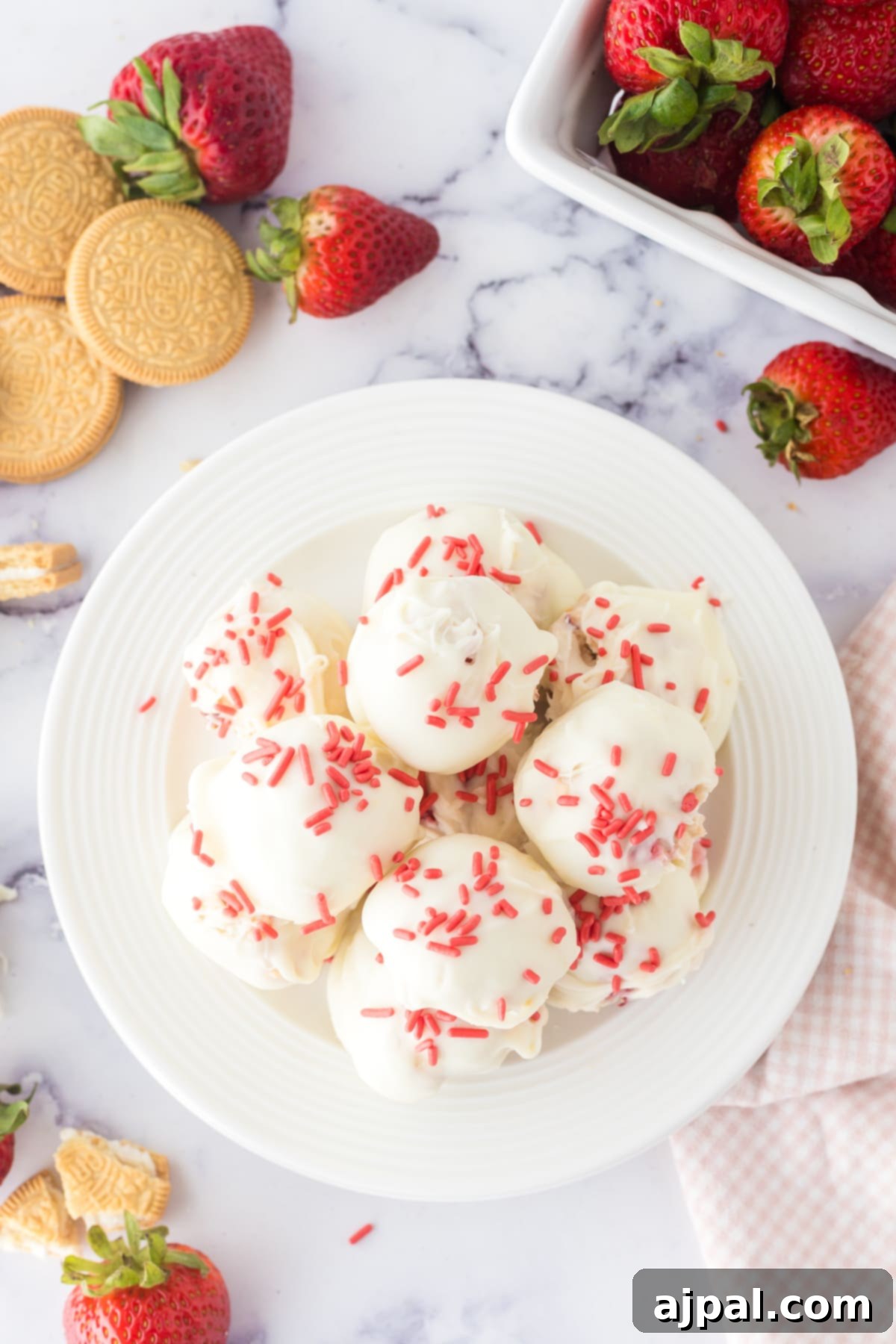 A stack of white chocolate-dipped strawberry shortcake truffles, embellished with pink sprinkles, presented on a pristine white plate.